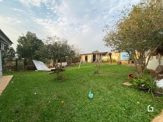 Vista externa de um gramado com árvores e estruturas ao fundo.