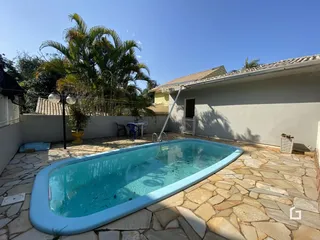 Foto da piscina externa em um quintal com vegetação tropical.