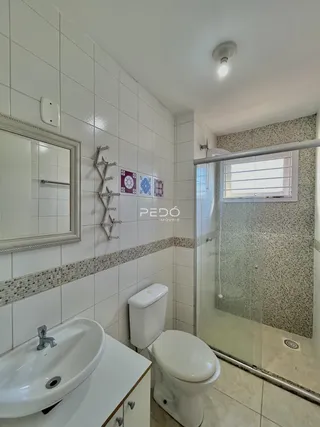 Banheiro com revestimento cerâmico branco e box de vidro.