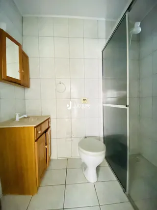 Foto interna de um banheiro com revestimento de cerâmica branca e armários de madeira.