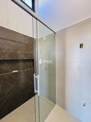 Interior de um banheiro com revestimento em tons de cinza e vidro.