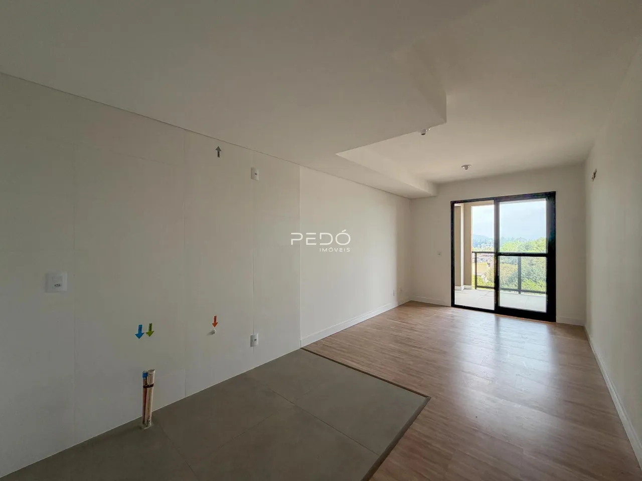 Ambiente interno de uma sala ampla com piso de madeira e parede branca.