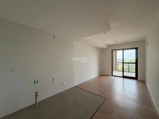 Ambiente interno de uma sala ampla com piso de madeira e parede branca.