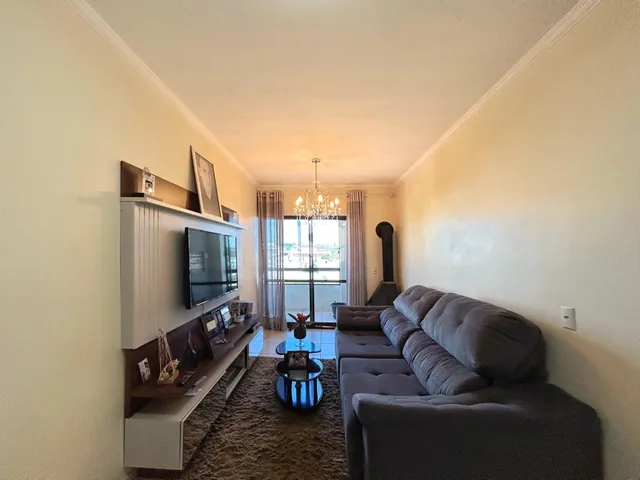 Sala de estar com sofá cinza e televisão em um apartamento em Lajeado.