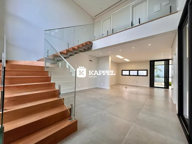 Vista interna de uma sala de estar moderna com escadaria de madeira e piso claro.