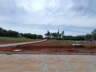 A foto mostra uma área de terra com uma estrada de terra e vegetação ao fundo.