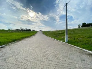 Vista de uma estrada pavimentada ladeada por campos verdes sob um céu nublado.