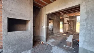 Interior de uma área em construção com paredes de concreto aparente e estrutura de teto de madeira.
