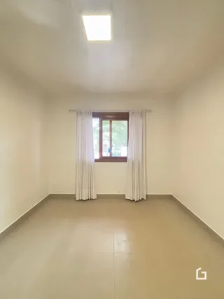 Foto de uma sala interna com uma janela e cortinas brancas.
