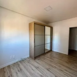 Foto de um corredor interno com piso de madeira clara e paredes brancas.