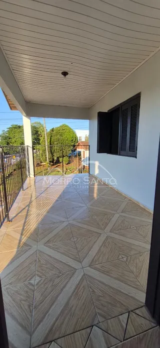 Vista de uma área externa coberta com piso de losa e estrutura de teto branco.