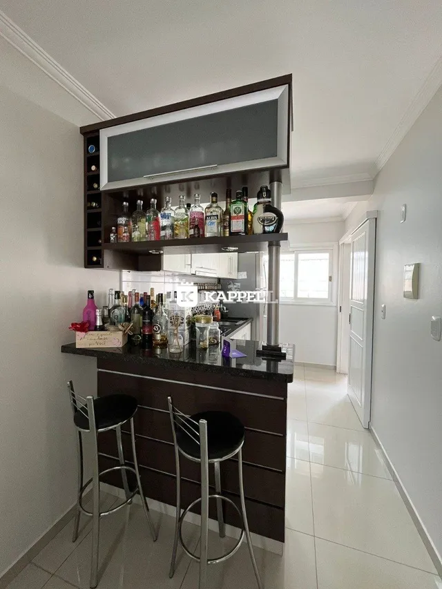 Bancada de cozinha escura com prateleiras de bebidas e banquetas.