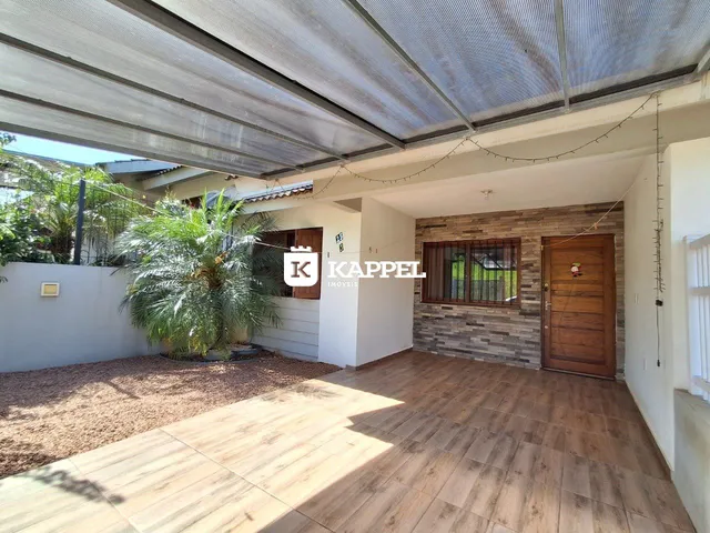 Área externa coberta com piso de madeira e vegetação ao lado de uma casa.