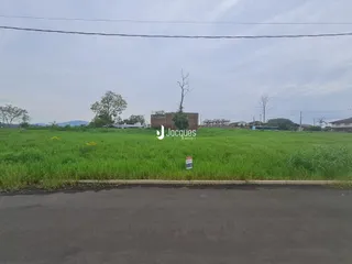 Vista externa de um terreno gramado com vegetação ao fundo.