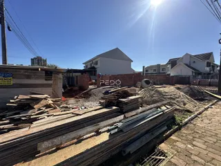 Vista de uma área de construção com pilhas de madeira e terra no primeiro plano.