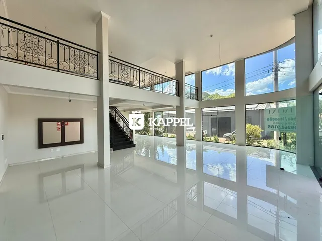 Vista interna de um espaço amplo com piso claro e grandes janelas.