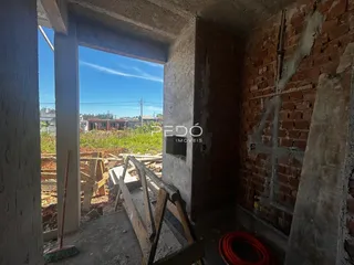 Vista interna de uma estrutura com paredes de tijolo aparente e abertura para uma área externa em construção.