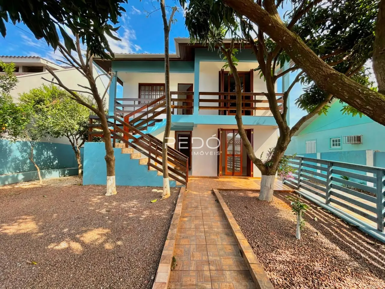 Fachada de uma casa azul em Lajeado, Brasil, com jardim e árvores ao redor.