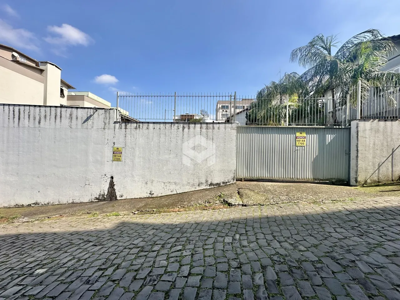 Vista da fachada de uma propriedade com muro e portão de metal.