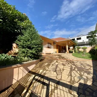 Vista externa de uma propriedade com pátio pavimentado e vegetação exuberante.