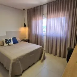 Quarto com cama de casal e cortinas claras.