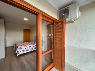 Vista interna de um quarto com cama e piso de madeira.