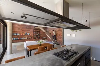 Interior de uma sala de estar com parede de tijolos aparentes e cozinha moderna.