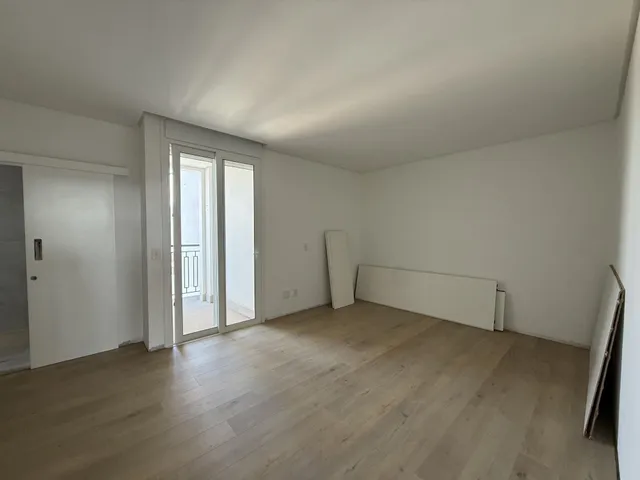 Uma sala ampla com piso de madeira clara e paredes brancas.