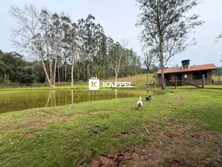 Paisagem externa mostrando um campo gramado, um lago e uma construção rústica ao fundo.