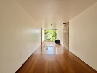Corredor longo com piso de madeira e janela no final da passagem.