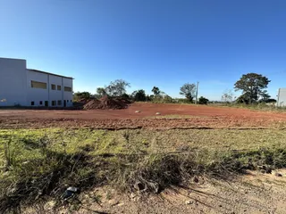 Foto de um terreno aberto com solo avermelhado e vegetação rasteira sob um céu azul.