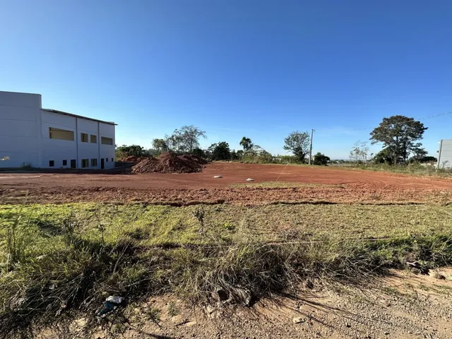 Foto de um terreno aberto com solo avermelhado e vegetação rasteira sob um céu azul.