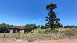 Vista externa de uma paisagem rural com vegetação seca e uma residência ao fundo.