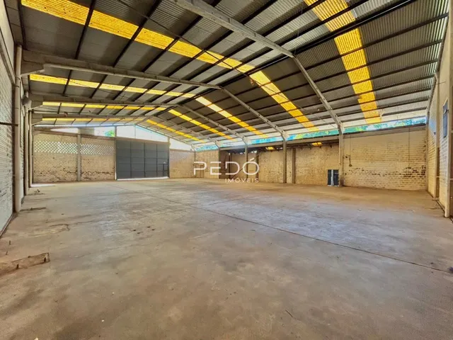 Vista interna de um grande espaço industrial com teto de metal e paredes de tijolo.