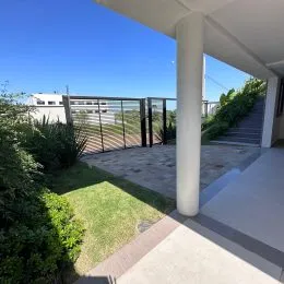 Vista externa de uma varanda com área verde e céu azul.