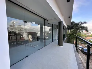 Vista de uma varanda moderna com piso claro e guarda-corpo de vidro.