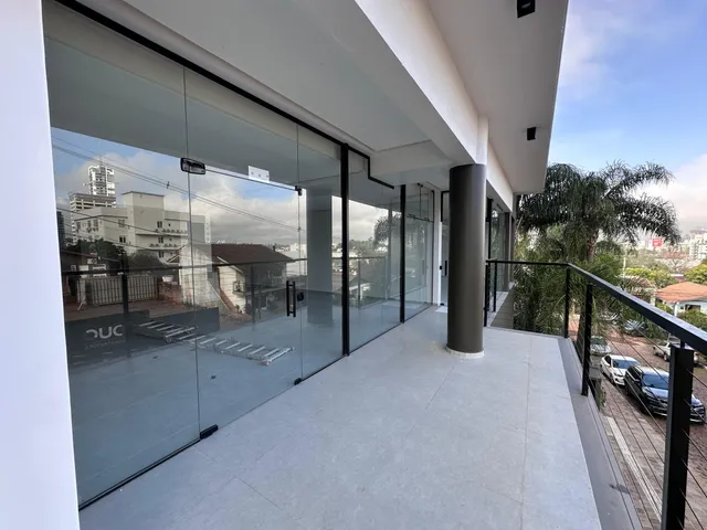 Vista de uma varanda moderna com piso claro e guarda-corpo de vidro.