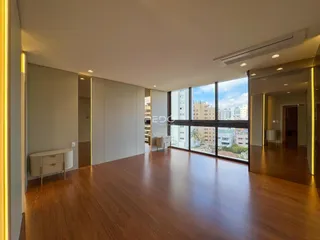 Sala de estar ampla com piso de madeira e grandes janelas que dão vista para a cidade.