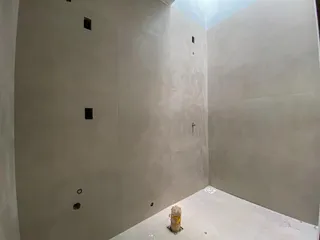 Vista interna de um espaço com paredes brancas e piso em obra.