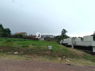 Vista da propriedade com terreno gramado e edificações ao fundo.
