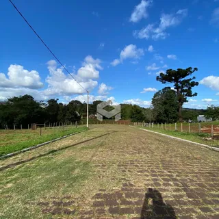 Vista de uma estrada gramada em uma área rural sob um céu azul com nuvens.