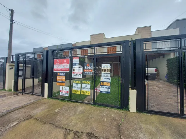 Vista externa de uma propriedade com portões de metal preto e placas de anúncio.