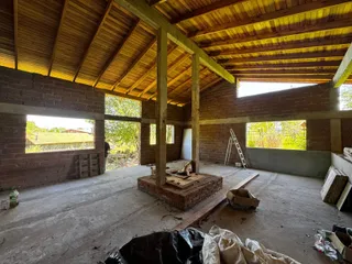 Foto do interior de uma estrutura em construção com paredes de tijolo aparente e forro de madeira.