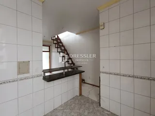 Vista de um corredor interno com paredes brancas e um lance de escadas.