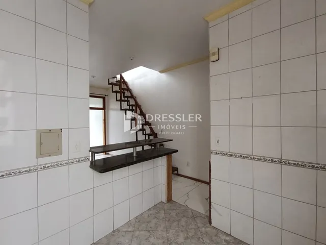 Vista de um corredor interno com paredes brancas e um lance de escadas.