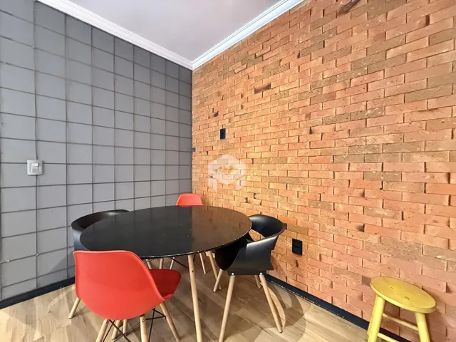 Uma sala de jantar com mesa redonda e cadeiras em um ambiente com parede de tijolos aparentes.