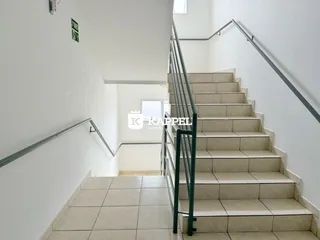 Foto de uma escadaria interna com degraus claros e corrimãos metálicos em um corredor.
