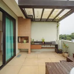 Vista de uma área externa coberta com estrutura de pergolado e piso claro.