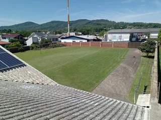 Vista externa de um jardim gramado com caminho de terra e telhado de telhas.
