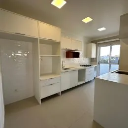 Foto interna de uma cozinha com armários brancos e bancada clara.